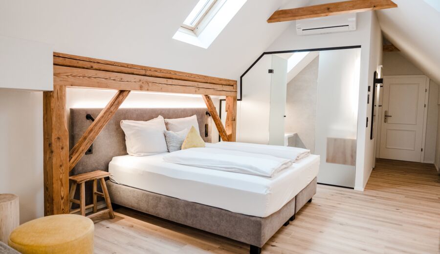 Ein Doppelbett das von der Seite fotografiert wurde und vom Dachfenster beleuchtet wird, während man die Schiebetür zum Badezimmer im Hintergrund erkennen kann