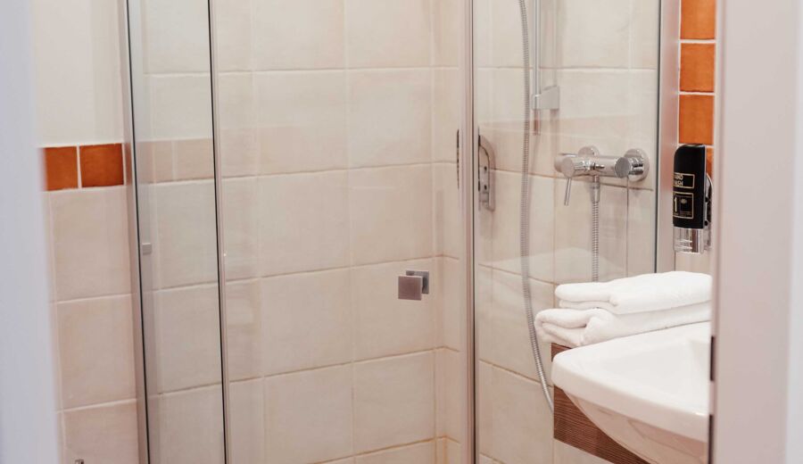 Durchsichtige Dusche im Badezimmer mit weißen und orangefarbenen Fliesen im Hotel Kirchbichl