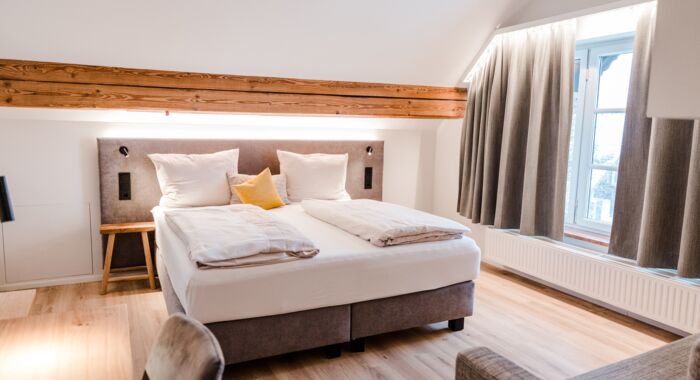 Ein gräuliches Bett mit weißer Bettwäsche das in der Mitte vom Bild steht