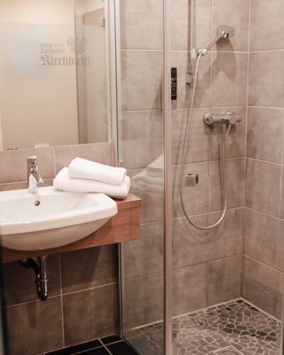 Eine Walk-In Dusche und ein Waschbecken im Badezimmer des Twinzimmers im 4-Sterne Hotel Kirchbichl