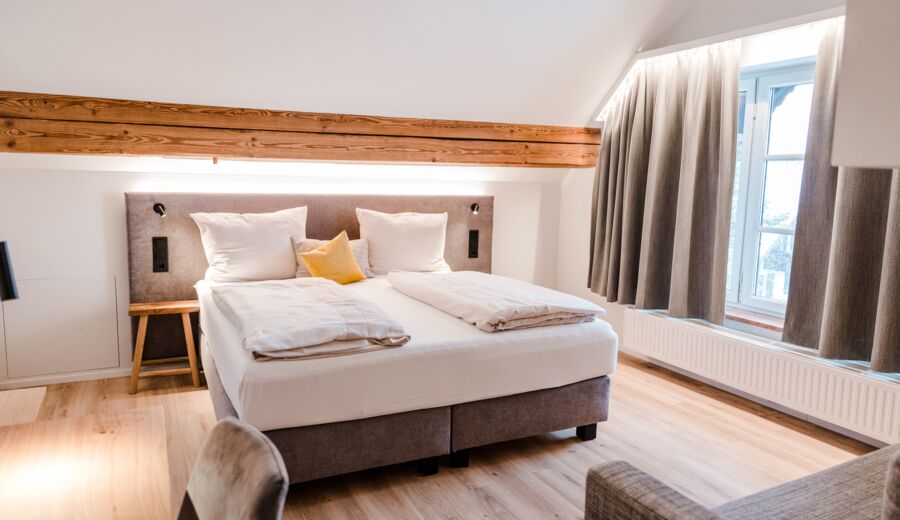 Ein gräuliches Bett mit weißer Bettwäsche das in der Mitte vom Bild steht