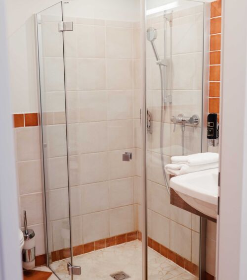 Durchsichtige Dusche im Badezimmer mit weißen und orangefarbenen Fliesen im Hotel Kirchbichl