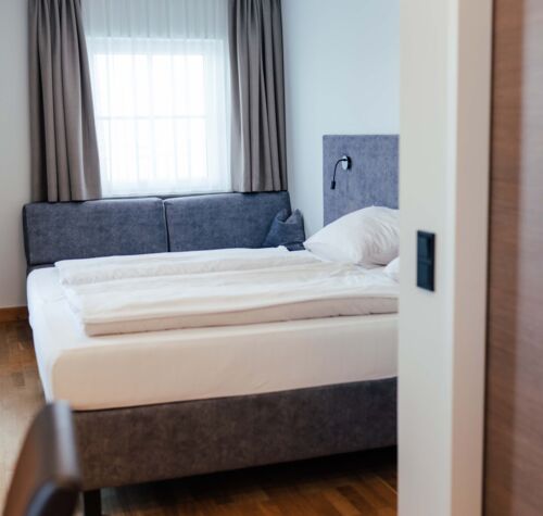 Ein Doppel Bett und eine Couch im Doppelzimmer des Landgasthofs Kirchbichl