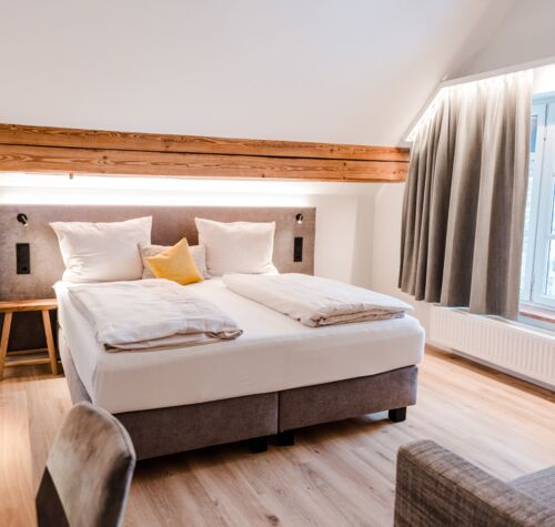Ein gräuliches Bett mit weißer Bettwäsche das in der Mitte vom Bild steht