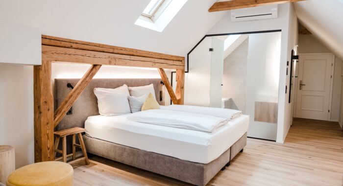 Ein Doppelbett das von der Seite fotografiert wurde und vom Dachfenster beleuchtet wird, während man die Schiebetür zum Badezimmer im Hintergrund erkennen kann