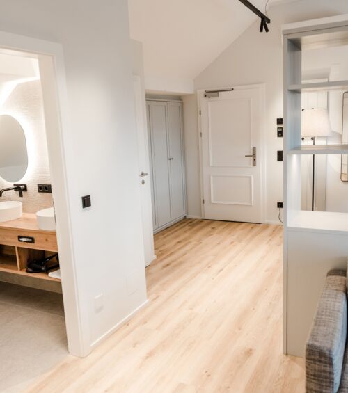 Ein Großraum Bild von dem Familienzimmer wo auf der rechten Seite die Couch und ein Schrank dahinter zusehen ist und auf der anderen Seite sieht man in das Badezimmer hinein.