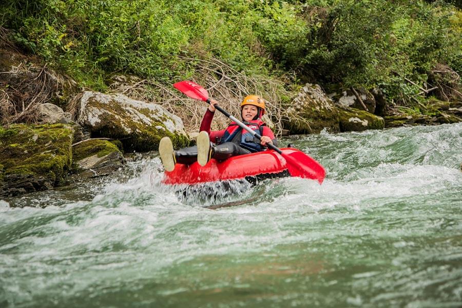 A girl rafts in a rubber boat in a river, a paddle, a life jacket and a helmet give her protection